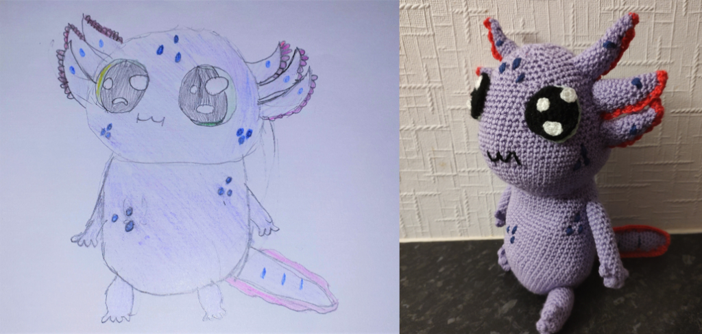 A child's drawing of a purple creature that looks like an axolotl, with Pokemon like face and black eyes with white highlight in them. The crochet toy is on the right.