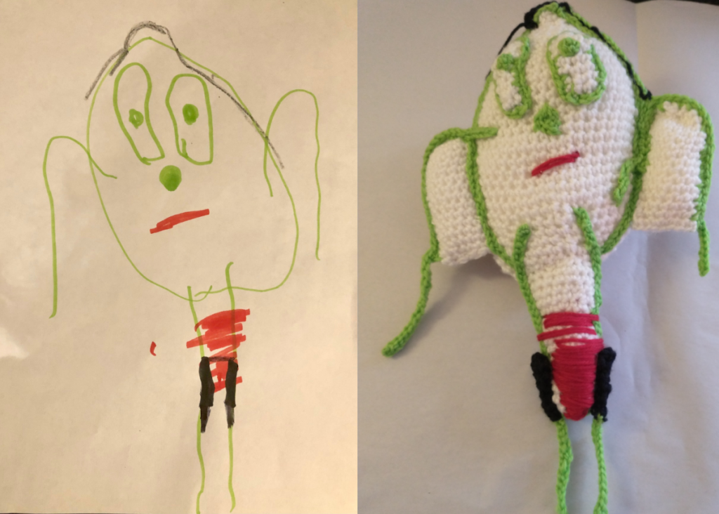 A photo of a young child's drawing of a man with a big white head, red shorts and skinny green arms and legs. The crochet doll of the drawing is on the left