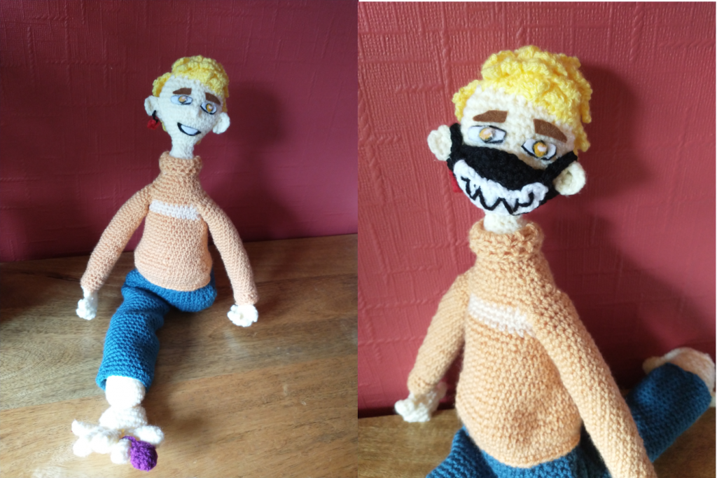 Two view of a crochet doll. In the first he can be seen smiling openly. In the second he is wearing a face mask over his mouth and nose which has jagged teeth sewn on it in black. He has curly yellow hair, yellow irises and thick, dark brown eyebrows. He is wearing an orange jumper and blue trousers