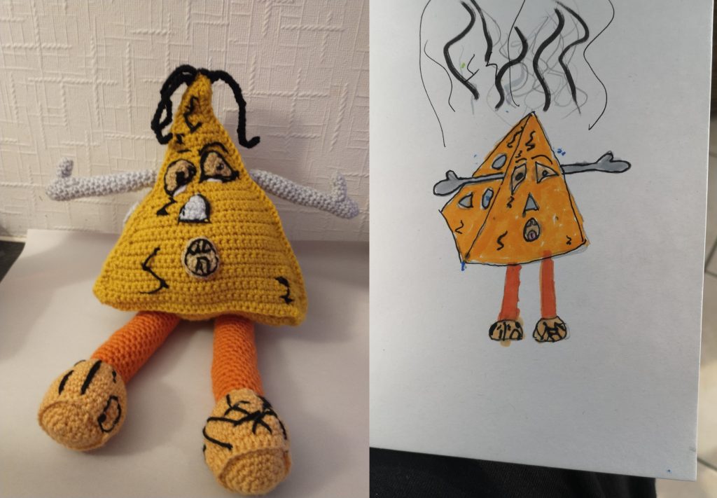 A crochet toy of a yellow triangular smelly cheese with black lines to represent the cheese bacteria. The drawing of the same is on the right with lines coming out of it to show how smelly it is