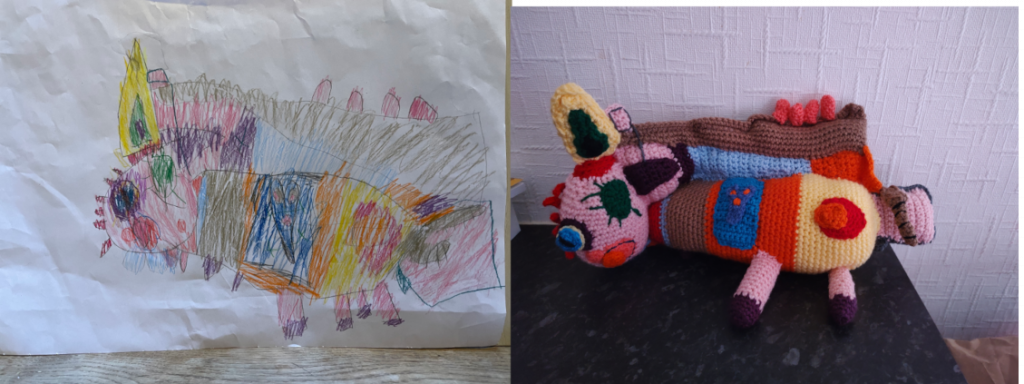 A child's drawing of a monster that is very multicoloured,with a pink face and green and blue eyes and an orange mouth and various colours on its body. The crochet toy is on the right.
