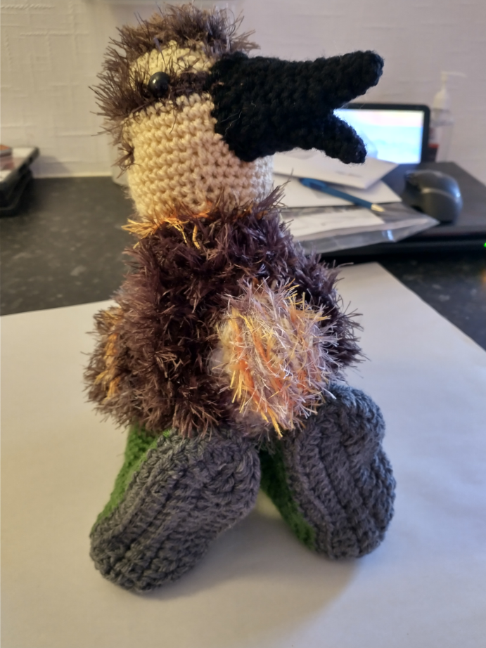 A crochet brown and yellow duckling wearing green wellies with grey soles