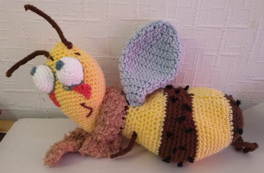 A photo of a crochet bee with a happy little face, wearing a fluffy brown scarf