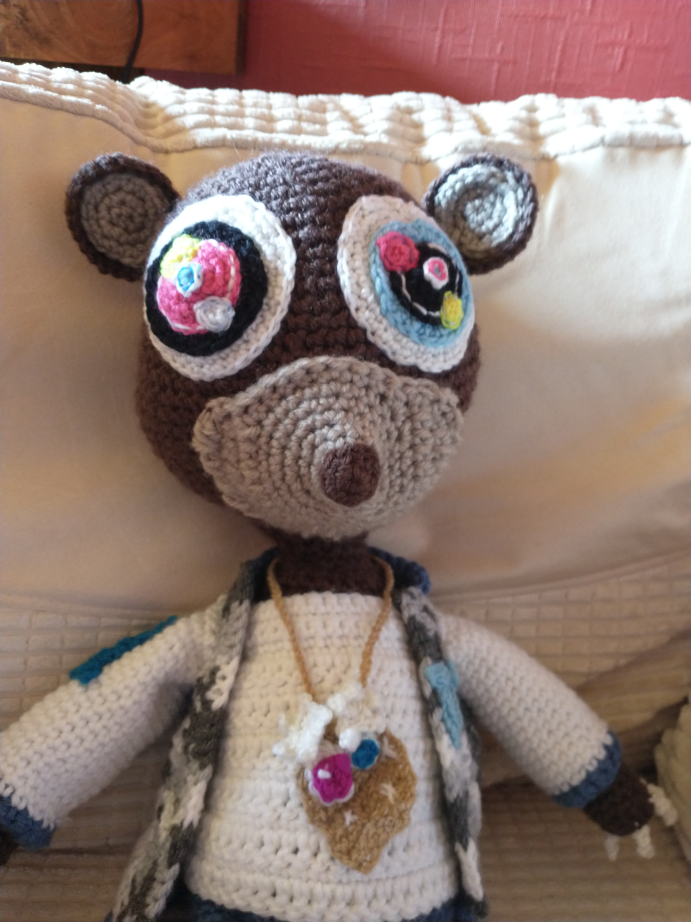 Crochet Bear with bright, multi-coloured eyes, sporting a white top and blue and grey camo jacket