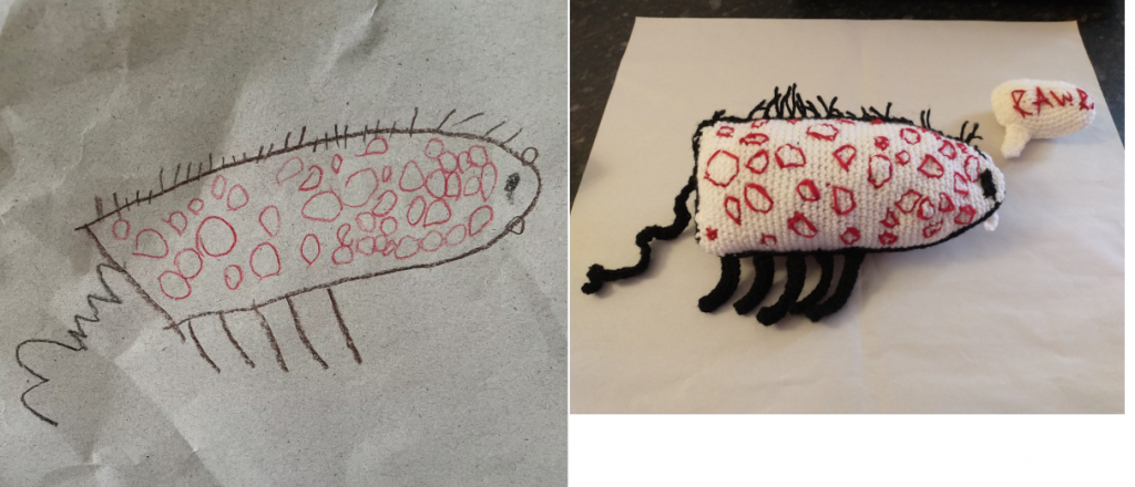 A photo showing a drawing of a short work-like creature with black hairs, five black legs and a white body with lots of red circles on it. On the right is the same creature made into a crochet toy with a speech bubble above its head and the word "RawR!" in red