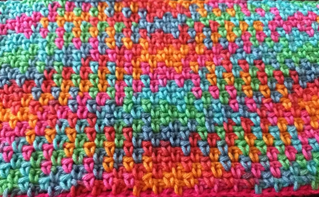 A photo of a colourful crochet piece in the Argyle pattern. The colours are green, blue, pink, orange and purple