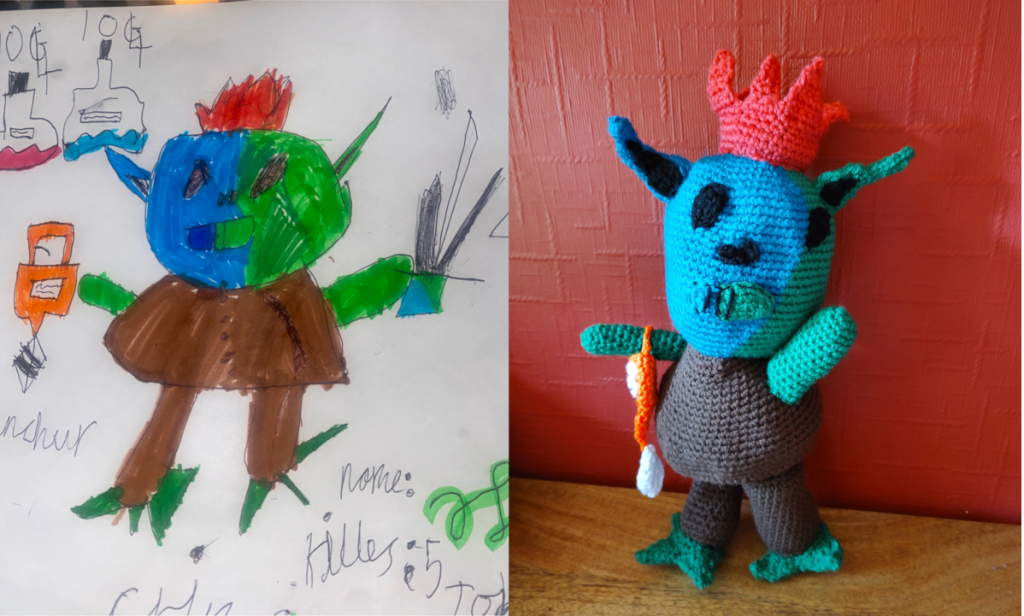 A photo of a child's drawing of a goblin like creature, which has a blue and green face from left to right, green arms and three green toes on each feet. It has black eyes and a mouth that is half green and half blue. It has one blue and one green pointed ear and it is wearing a pink-orange crown. It is holding an orange bag like creation with a white label on it. It is wearing a dark brown tunic and trousers. Next to the drawing is a photo of the crochet toy made from the drawing