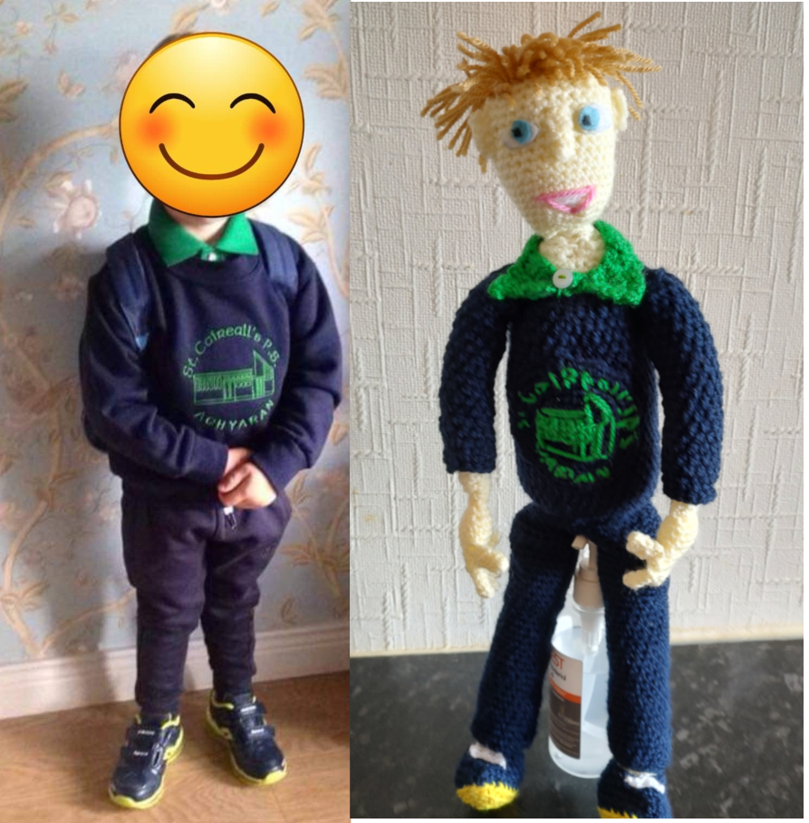 A photo of a boy in a school uniform with a cartoon smiley face protecting his identity. On the right is the crochet doll. He is wearing a navy blue jumper with a green school logo across the front, and a green shirt. he has on navy trousers and blue and yellow athletic shoes. He has short light brown hair, blue eyes, and is wearing a large smile