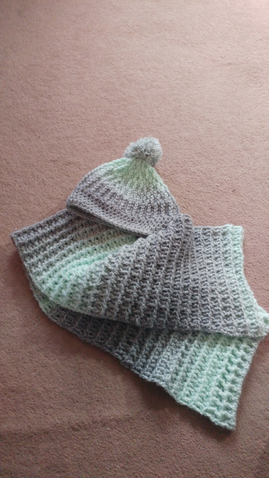 A photo of a mint green and grey crochet hat and scarf. Both are ribbed and the hat has a pom pom on the top