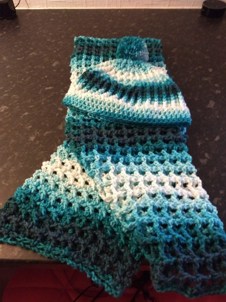 A photo of a blue and white variegated, ribbed crochet hat and scarf. the hat has a bobble on the top