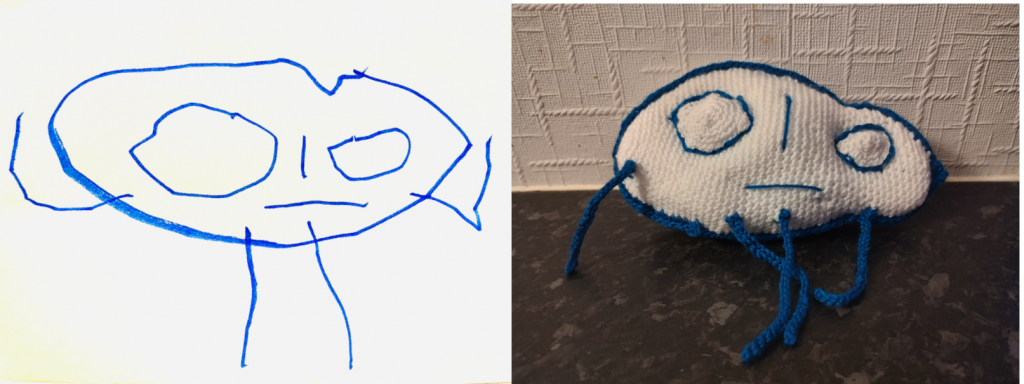 An outline drawing of a stick figure with a large white oval head and two large oval eyes outlined in blue. The crochet toy is on the right.