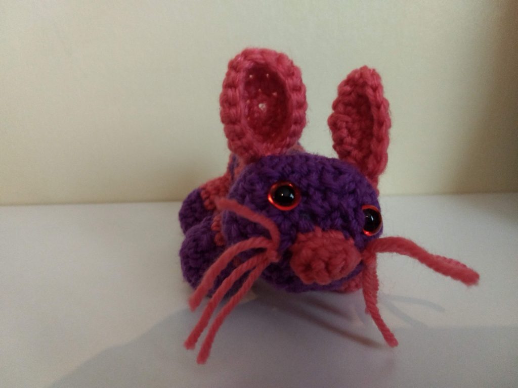 A photo of the purple and pink crochet mouse. He has long pink whiskers and pink nose and ears