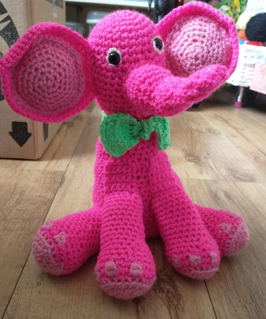 A close up image of the same pink elephant sitting on a laminate floor.