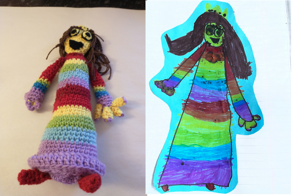 A crochet princess doll on the left next to a child's drawing on the right of the same. The princess has a rainbow coloured stripy dress on and red shoes. She has large yellow fingers on one hand and smaller ones on the other. She has a yellow face, a large black smiling mouth and eyes and long brown hair and is wearing a yellow crown