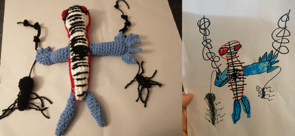 A photo of a crochet spider man toy on the left and a child's drawing of spider man on the right. He has a long white body with webs cross it and a spider in the middle and blue arms and legs. He has two red eyes and his body is outlined in red. He is holding webs and a spider in each hand.