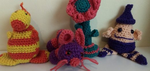A photo of four small crochet toys. From left to right: A little figure in orange and yellow strips with tiny flippers an a large nose, a mouse in pink and purple, a flower in green and pink and a little wizard-like character in cream and purple with a purple hat