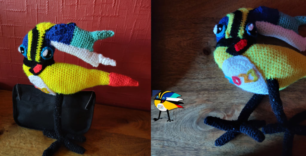 Two side by side photos of a crochet toy that has been made to look like the Olympic logo for Santiago Chile in 2023. The logo is a bird with a yellow body, red tail, black legs and head feathers in blue, yellow, black, blue again, lighter blue and white, swept back from it's front facing head. The eyes are bug and blue with white reflections in the pupils. The mouth is open and red. On the chest is writing. In the crochet toy this is just the year in multiicolour letters.