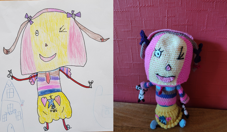 A child's drawing of a little girl on the left, with the crochet toy made from it on the right. the little girl has a large oval head with a yellow face and pink sides. She has a large smiling pink mouth, little triangular pink node and one open green eye with black lashes. The other eye is closed in a wink. She has red skinny arms, a stripey pink, blue and purple top and a red tie. She has a fluffy yellow skirt with two pink hearts and a blue star and small flower on it. She has skinny red legs and blue shoes. She is holding two small animals, one in each hand and she has pink hair with purple bows in it.
