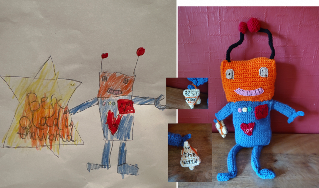 A child's drawing of a robot holding a large yellow star that says "Best Dad in the World" on it. The robot is blue with blue legs and arms and a square orange head with two ariels with red round bobbles on them. It has two square eyes which are a light pink colour and also a smiling mouth of the same colour full of robot teeth. It has a red square patch on its right breast with a wavy line on it like a EKG line. It has a red heart underneath this on the left with the word "Love" on it. Next to the drawing is a photo of the crochet toy version of the robot which is holder a much smaller star. The wording on the star is in two inserts showing the back and front which say "Best dad" and "in the world" respectively.