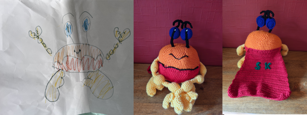 A child's drawing of a crab with two photos of the crochet toy version to the right. The crab has a shell split between red at the bottom and orange on the top. It has yellow arms made up of three ball like protrusions, and yellow crab claws. It has big yellow clawed feet and two blue eyes on black stalks with raise black eyebrows. It is smiling. On the right is the crochet toy facing forwards with its arms folded in front of it and next to this the same toy with its back facing the camera, showing a long red cloak with the letters "S" and "K" on it in green.