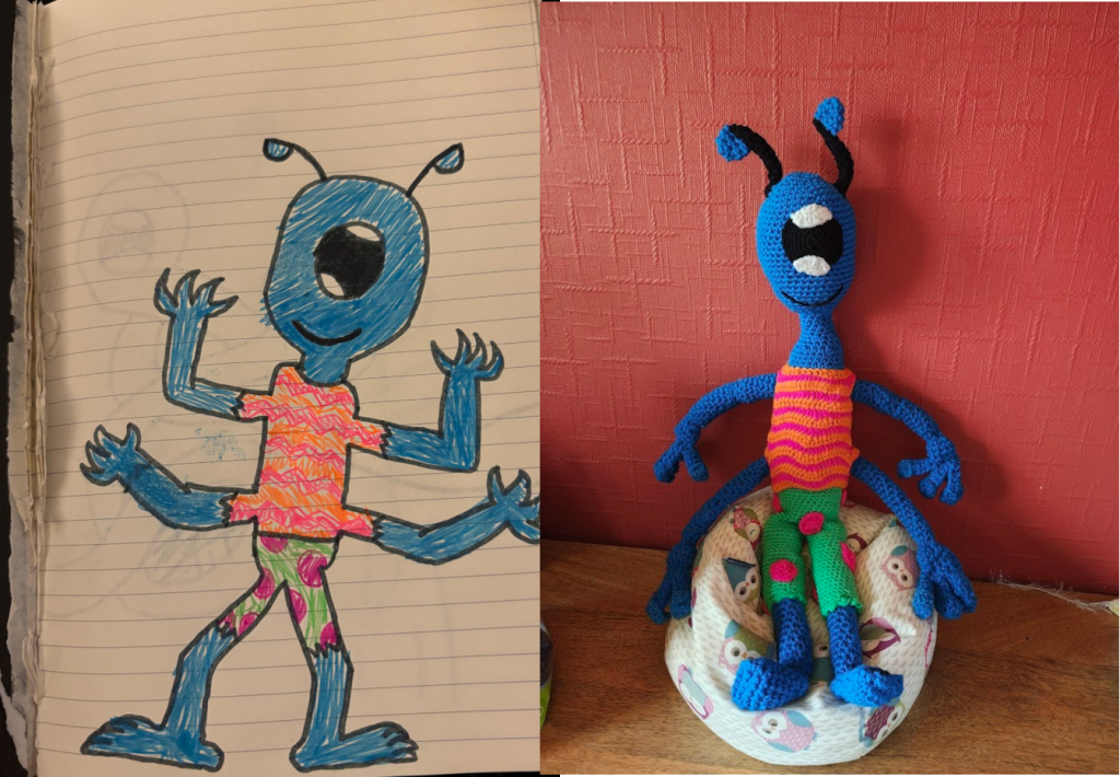 A child's drawing of a blue alien. He has a large oval head with two black tentacles with blue half circle tips and one large oval eye in the centre. It is black with white highlights on the top and bottom. He is wearing an orange and pink wavy line tank top and green trousers with pink spots. He has four thin blue arms with four fingers on each and two blue legs. His blue feet are bare. On the right is the crochet toy version of the drawing sitting on a little owl beanbag next to a red wall.